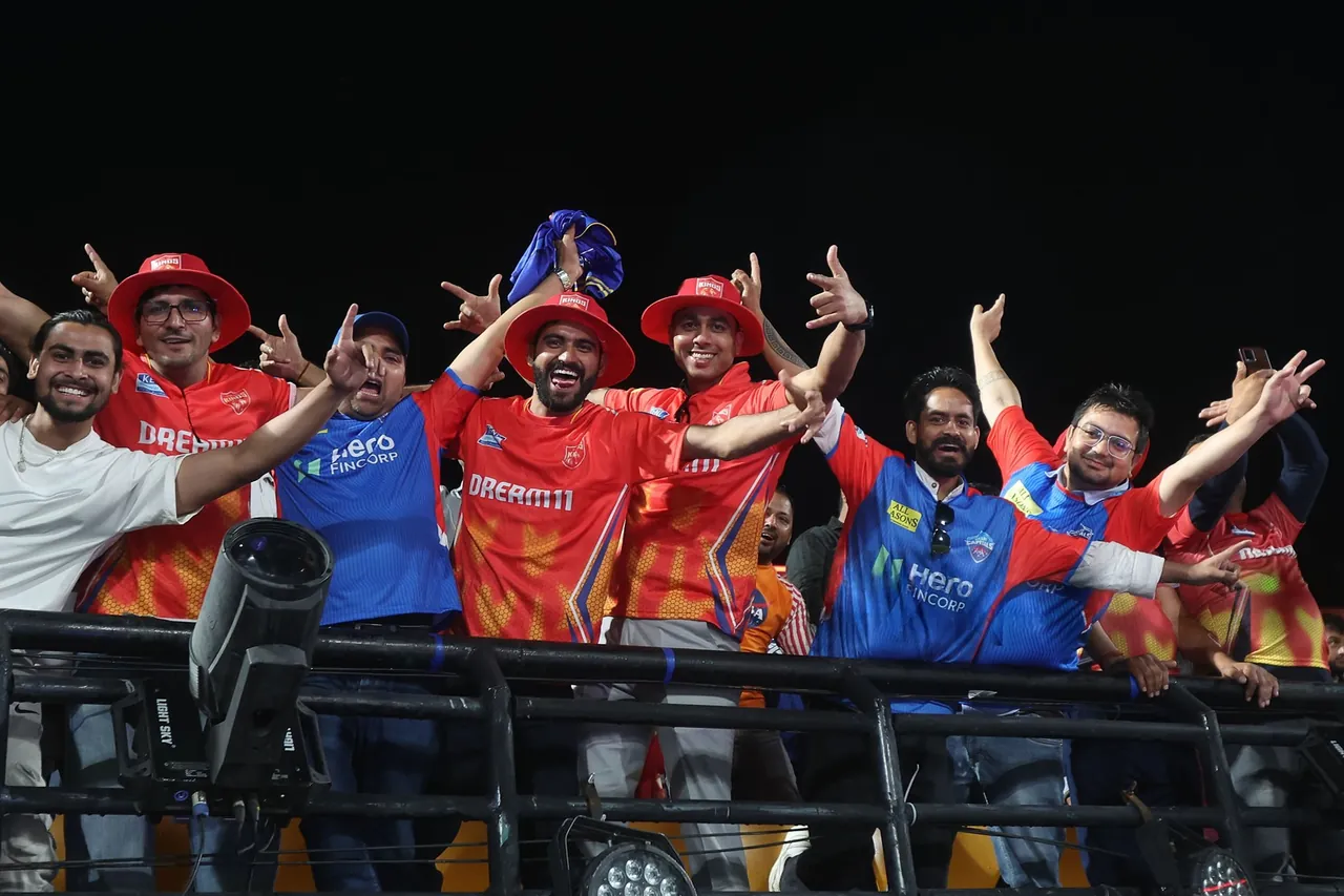 Cricket fans in team shirts cheering together at a night match in India