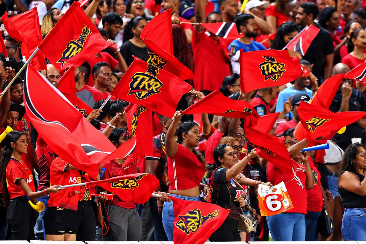 A crowd of cricket fans in red waving flags at a Caribbean match