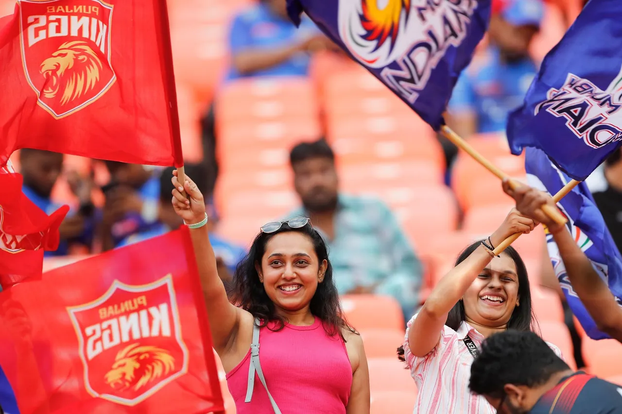 Two cricket fans smiling and waving team flags at a match in India